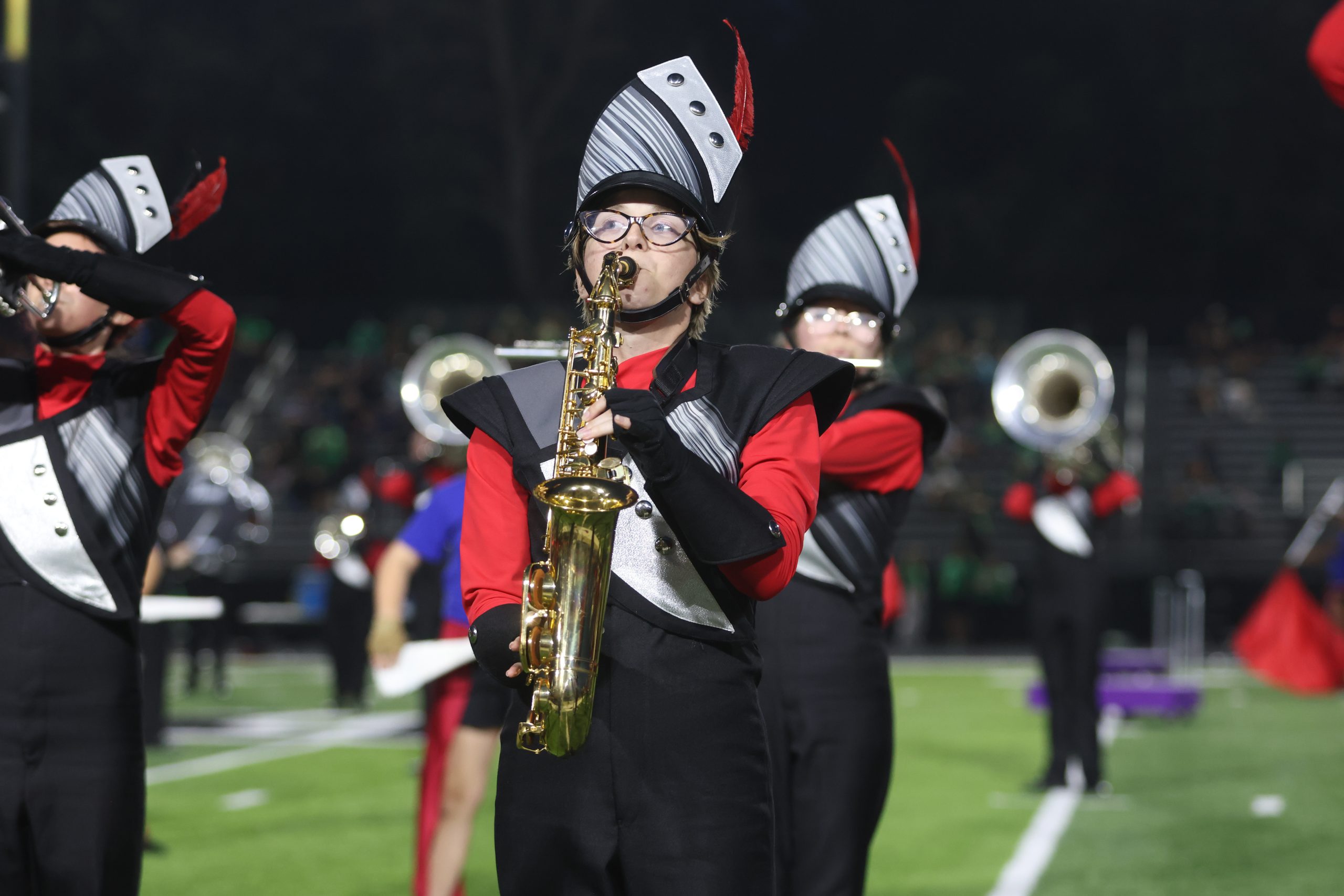 A group of marching band members performing on a football field at night.