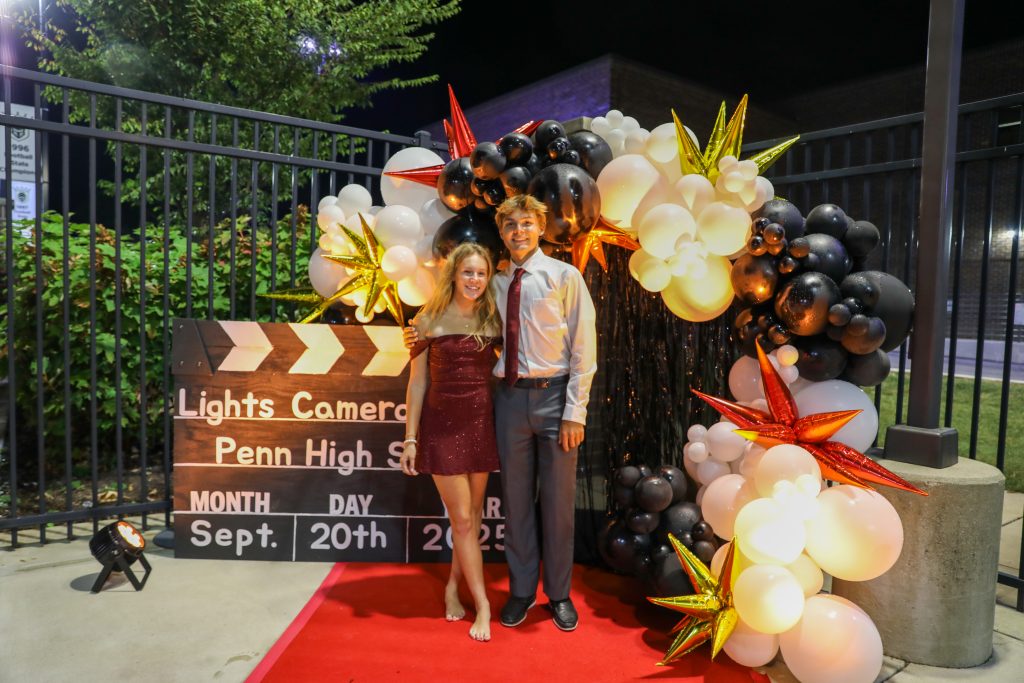 Two people standing in front of a balloon arch at a movie premiere.