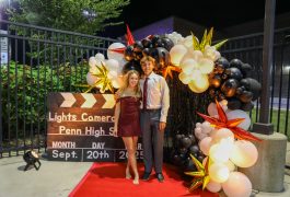 Two people standing in front of a balloon arch at a movie premiere.