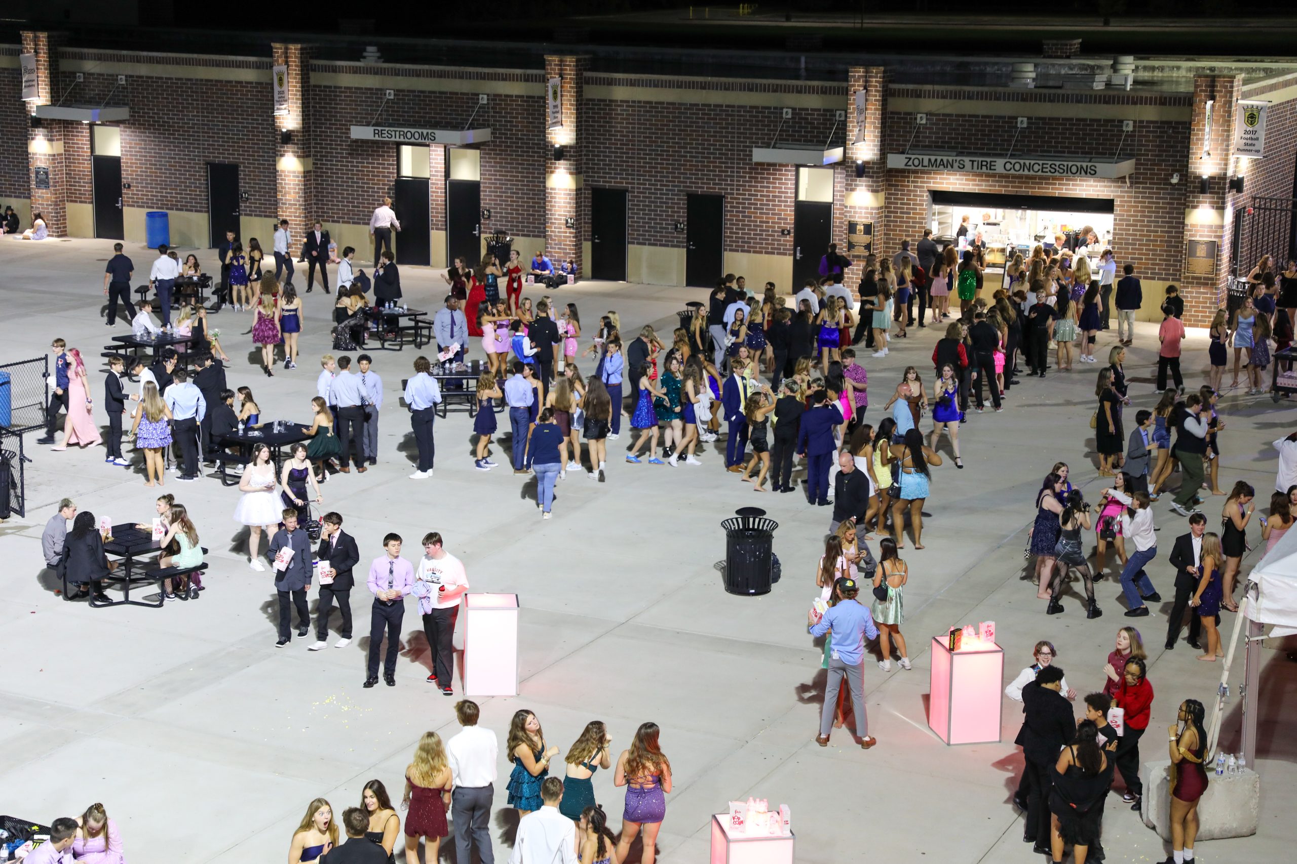 A lively scene at a nighttime event with people standing and socializing in a large open area, some with drinks, under a