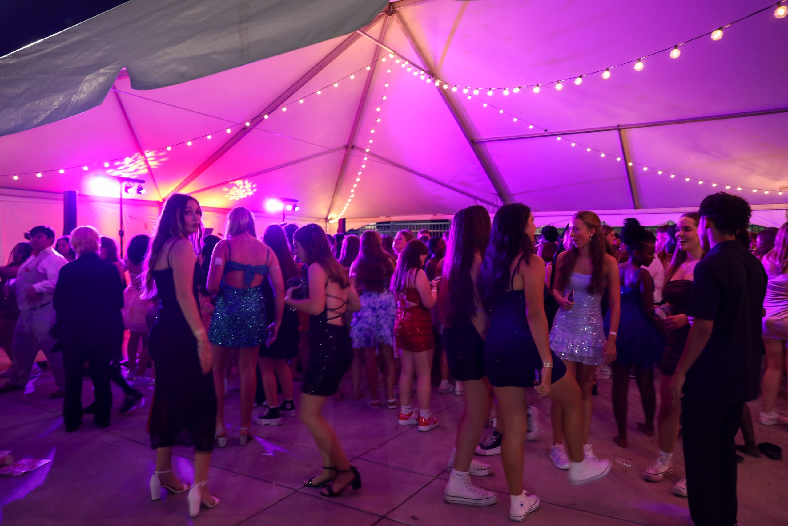 A group of people gathered at an outdoor event under a tent, with some standing and others dancing, all enjoying the festive