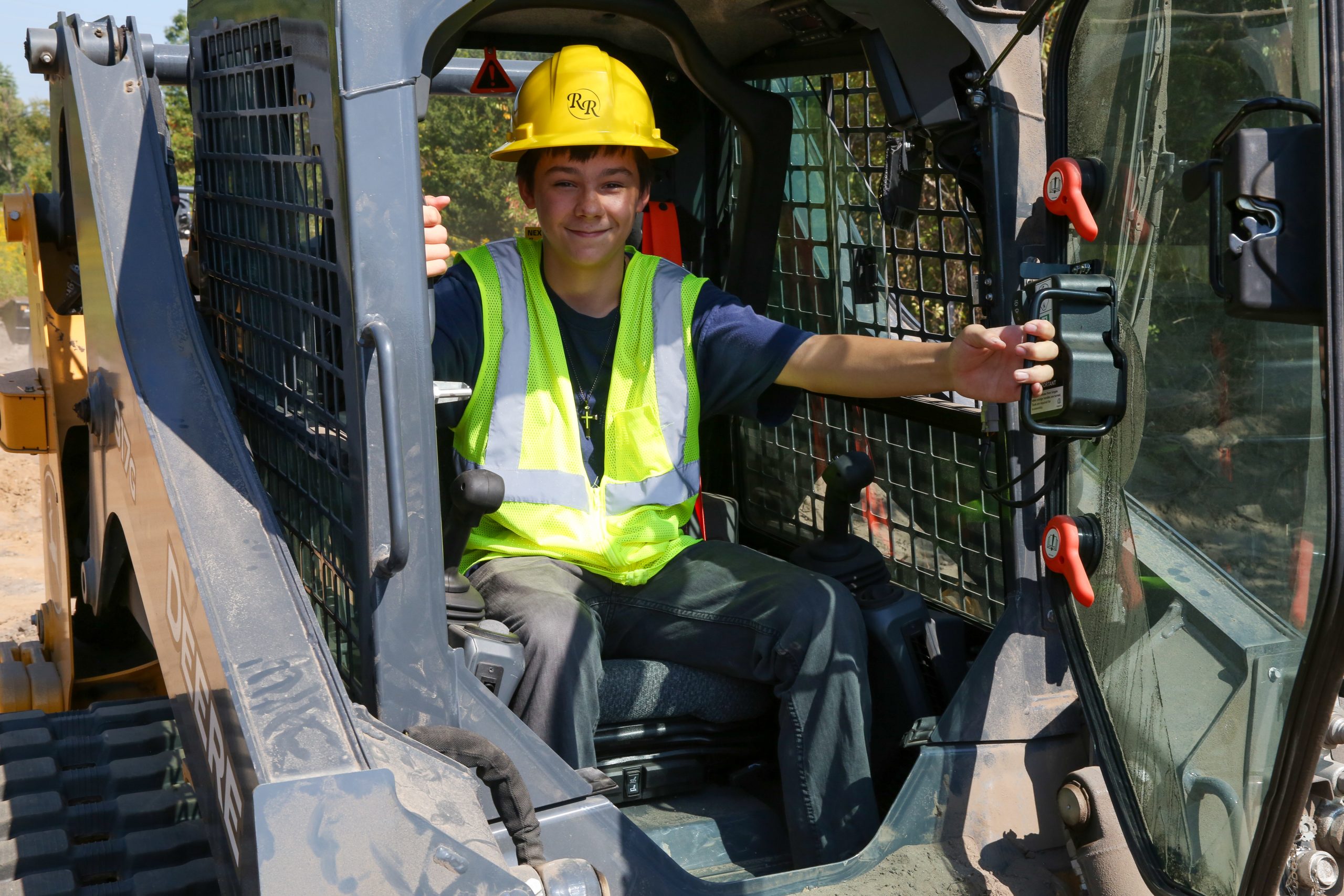 A person in a yellow safety vest is sitting inside a large piece of construction equipment.