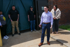 Man in suit standing outside building, giving speech to group of people.