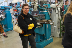 Woman in black sweater standing in front of industrial machinery in workshop.