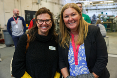 Two women standing in an industrial setting, smiling at the camera.