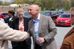 Man in suit shaking hands with others at outdoor event.